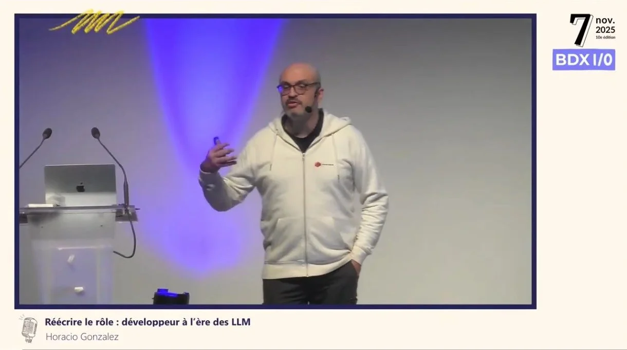 Horacio sur la scène de BDX I/O le 7 novembre 2025, en sweat blanc, pendant son talk « Réécrire le rôle : développeur à l'ère des LLM »